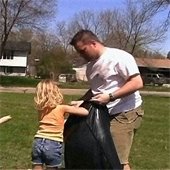 A child throws garbage in the bag an adult is holding.