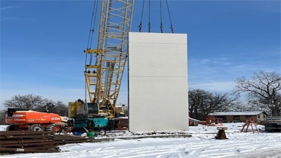 Yellow crane holds gray wall to put into place on snowy ground