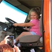 Child poses for photo holding the steering wheel of a big truck
