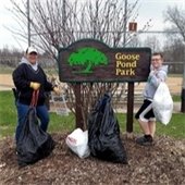 Two volunteers holding trash bags near the sign for Goose Pond Park