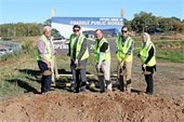 Group of 5 people in yellow construction vests holding shovels with dirt stand behind mound of dirt in front of large sign that reads "FUTURE HOME OF OAKDALE PUBLIC WORKS"