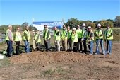 Group of 13 people in yellow construction vests holding shovels with dirt stand behind mound of dirt in front of large sign that reads "FUTURE HOME OF OAKDALE PUBLIC WORKS"