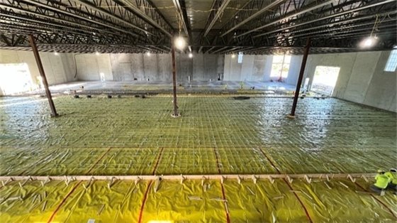 four people in bright yellow and orange construction vests stand in a building under construction with fresh concrete on the elevatedfloor