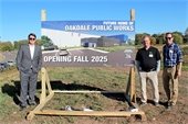 One man stands to left and two men to the right of a large sign on wooden frame that reads "FUTURE HOME OF OAKDALE PUBLIC WORKS OPENING FALL 2025"