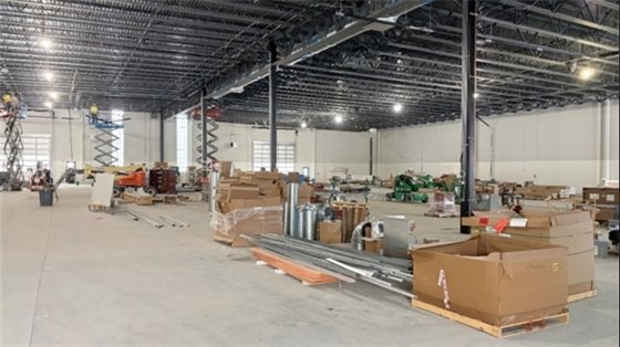 interior of a building under construction with large concrete floor and exposed silver metal beams on ceiling with many brown boxes in large open space 