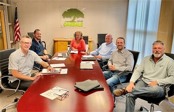 Members of the Public Works facility project team gather around a table with two males seated to the left, a woman in the center and three males on the right