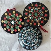 Three black rocks with colorful painted dot designs with two with red ribbons