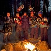 Group of women hold snowshoes by bonfire